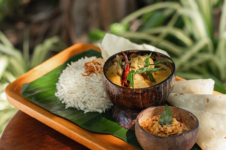 Holztablett mit Reis, einer Schüssel Curry und einem Löffel, typisch für die maledivische Küche.