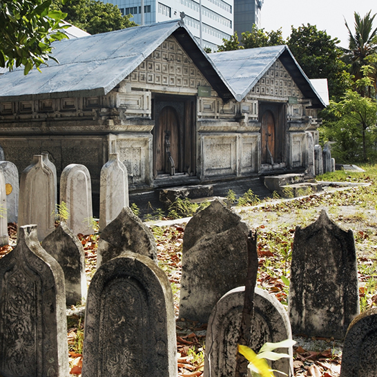 Ein Friedhof mit vielen Grabsteinen und einem Gebäude im Hintergrund, umgeben von der ruhigen Atmosphäre der Malediven.