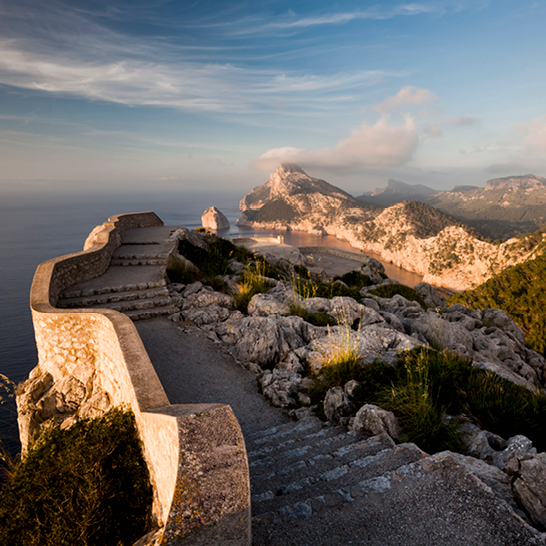 Blick vom Felsen auf das Meer und die Berge am Cap de Formentor, mit klarem Himmel und sanften Wellen.