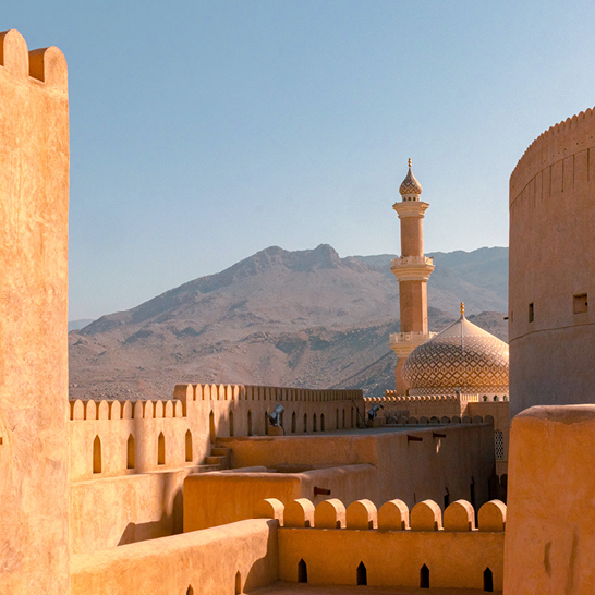 Blick von einem Gebäude in Nizwa, Oman, mit einer weiten Aussicht auf die Stadt und die umliegenden Berge.