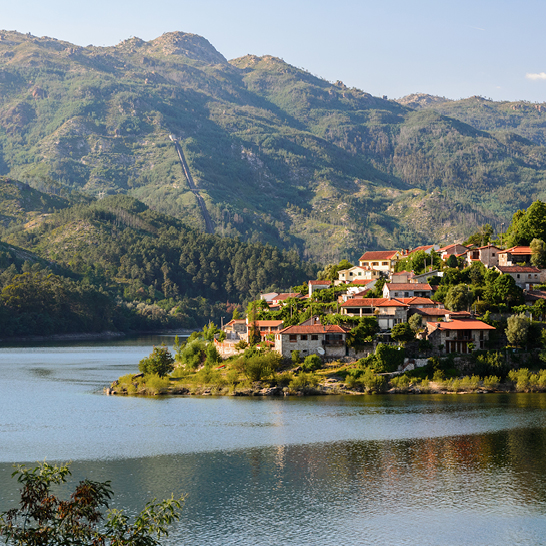 Ein kleines Dorf am Ufer eines Sees, umgeben von sanften Hügeln und Bäumen.