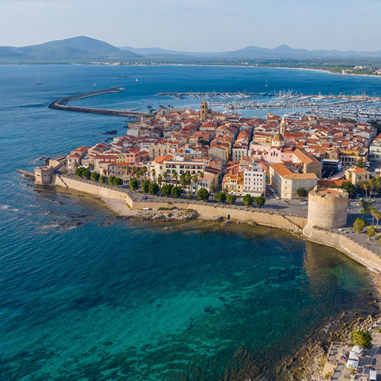 Ein ruhiger Wasserbereich in Alghero, umgeben von sanften Wellen und einem klaren blauen Himmel.