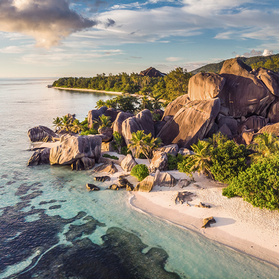 Luftaufnahme eines Strandes und Felsen in den Seychellen, mit klarem Wasser und üppigem Grün im Hintergrund.