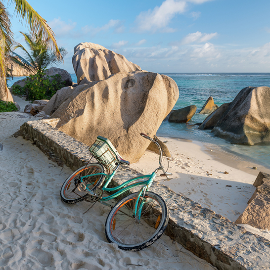 Am Strand der Seychellen parkt ein Vélo neben einem imposanten Felsen.