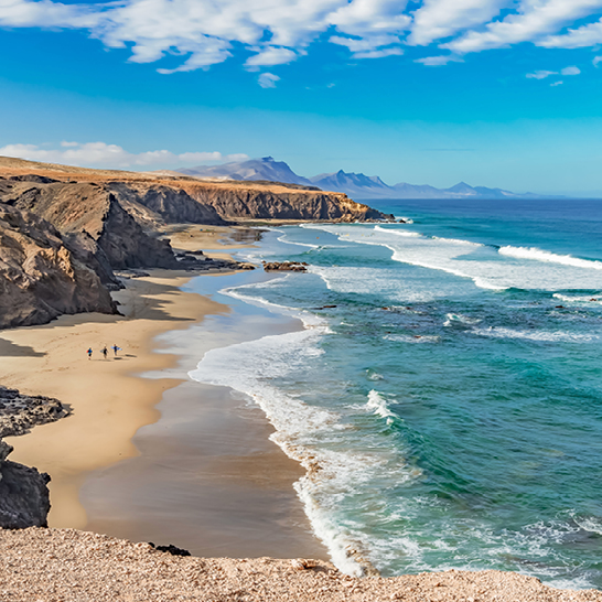 Strand in Spanien mit sanften Wellen und einer beeindruckenden Klippe im Hintergrund.