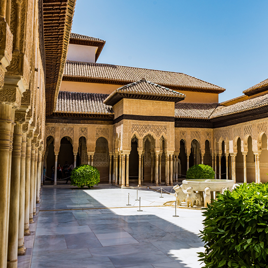  Innenhof der Alhambra mit einem Brunnen und einer Statue, umgeben von historischen Mauern und Pflanzen.
