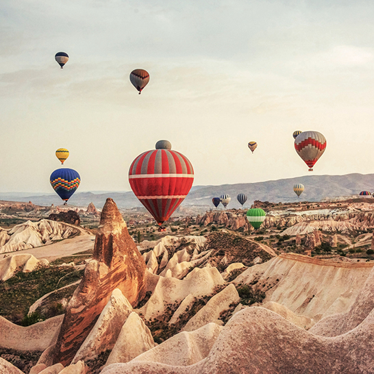 Viele Heissluftballons schweben über die felsige Landschaft von Kappadokien.