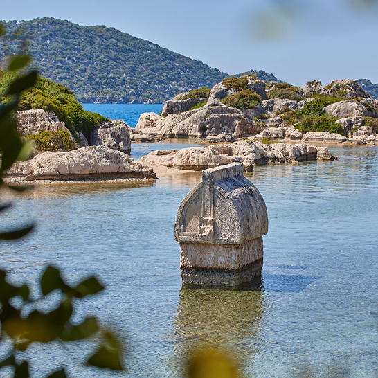 Ein Boot schwimmt im Wasser nahe der Felsen vor der Kekova Insel.