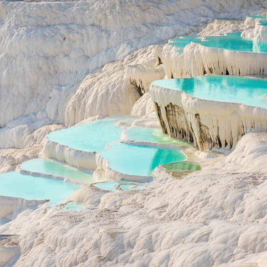 Blick auf die beeindruckenden Kalkterrassen von Pamukkale, Türkei, mit einem traditionellen türkischen Bad im Vordergrund.