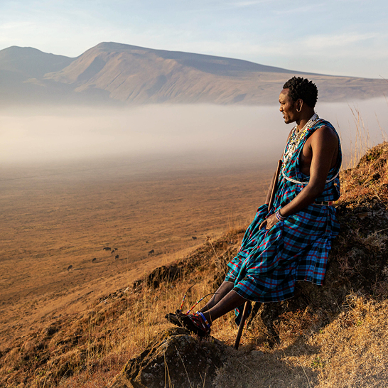 Eine Frau sitzt auf einem Felsen inmitten eines Feldes in Tansania, umgeben von grüner Landschaft.