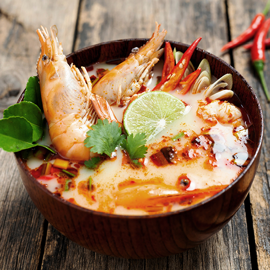 Thailändische Suppe mit Garnelen und buntem Gemüse in einer Schüssel serviert.