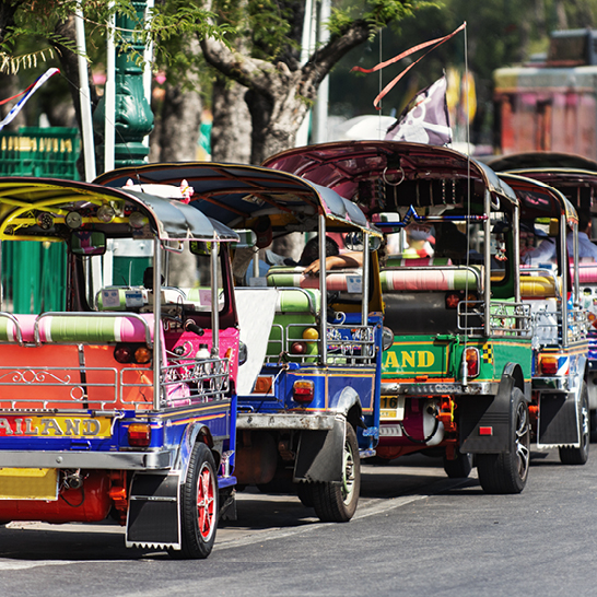 Eine Gruppe bunter Tuk-Tuks auf einer belebten Strasse in Thailand.