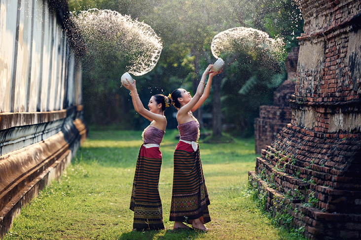 Zwei Frauen in traditioneller thailändischer Kleidung halten Blumen in den Händen und lächeln fröhlich.