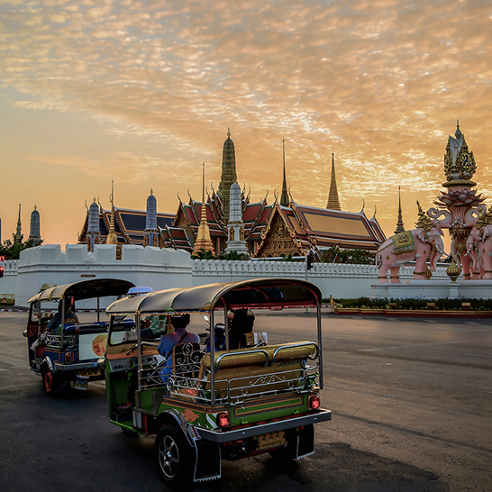 Zwei Tuk Tuks parken auf einer Strasse in Bangkok, Thailand, umgeben von urbaner Architektur und lebhaftem Stadtleben.