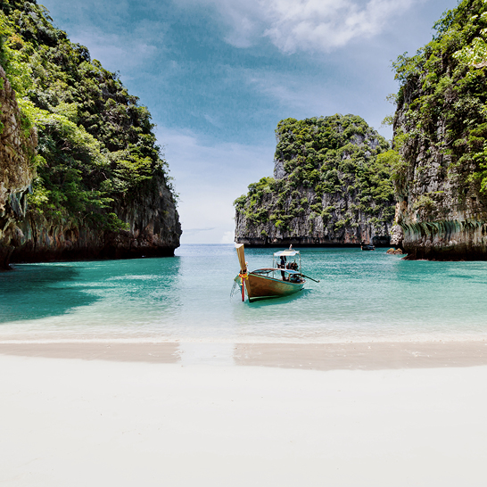 Ein Boot liegt am Strand nahe einer felsigen Küste in Phuket, Thailand, mit Blick auf die Koh Phi Phi Inseln.