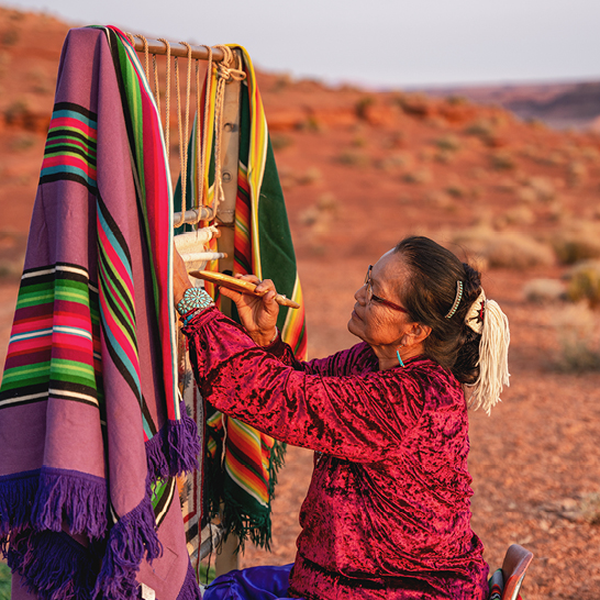Eine Frau webt eine Decke auf einem Holzrahmen im Wilder Westen, USA.