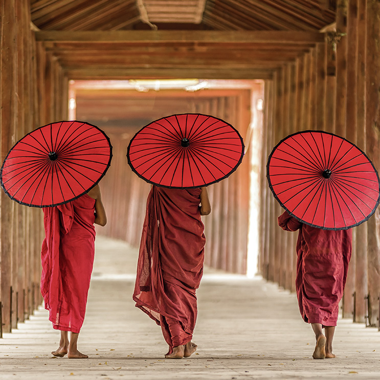 Asiatische buddhistische Mönche in roten Gewändern, die einen Sonnenschirm tragen, um sich vor der Sonne zu schützen, in einer friedlichen und spirituellen Umgebung.