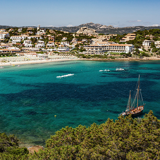 Baia Sardinia: Ein weitläufiges Gewässer, umgeben von einem schönen Strand und grünen Bäumen.
