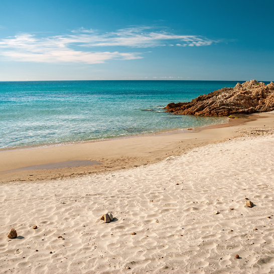  Ein Strand in Santa Margherita di Pula, Sardinien, mit Felsen und klarem Wasser.
