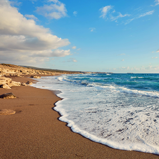 Schöner goldener Sandstrand mit Wellen in Paphos, Zypern.